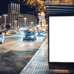 pannello pubblicitario sul marciapiede di una strada trafficata di sera